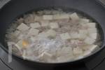 小さめのフライパンに水と割烹白だしを入れて中火にかけ、沸騰してきたら豆腐を加える。再び沸騰してきたらひき肉をほぐしながら加える。